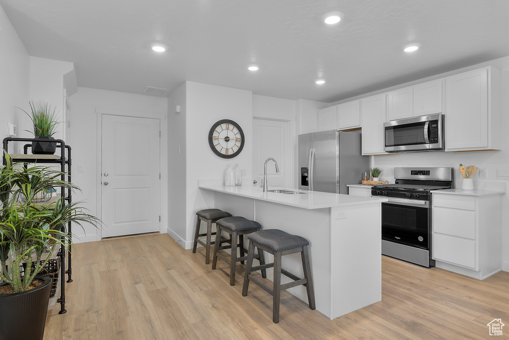 Kitchen with a sink, a breakfast bar, appliances with stainless steel finishes, light wood-style flooring, and white cabinets