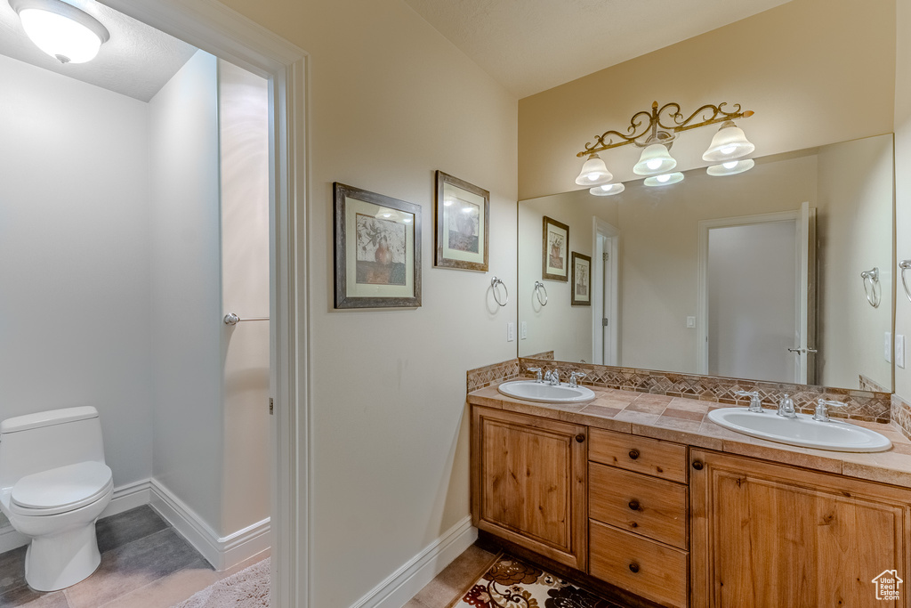 Bathroom with baseboards, double vanity, a sink, and toilet