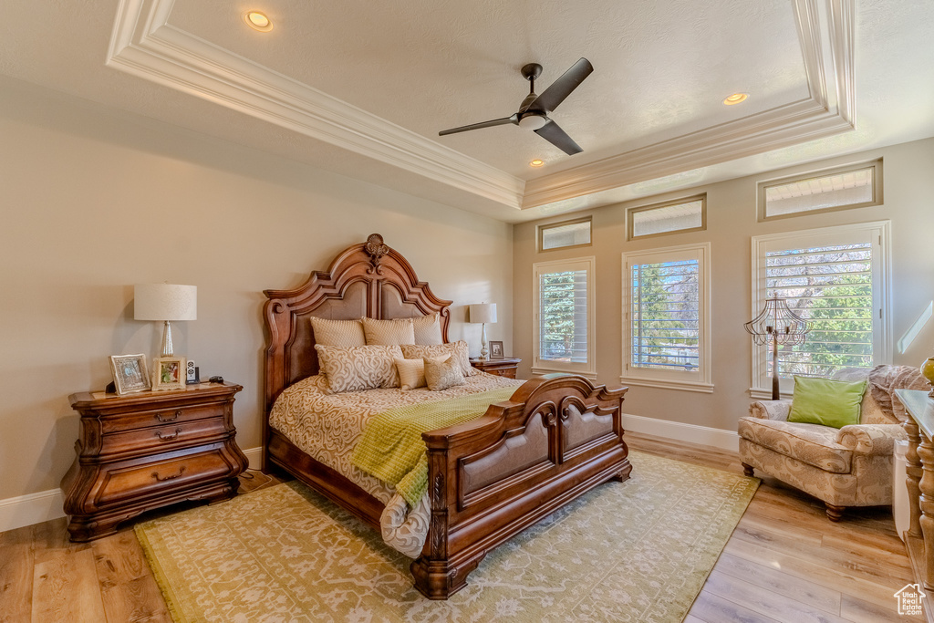 Bedroom featuring baseboards, light wood-style floors, ornamental molding, and a raised ceiling