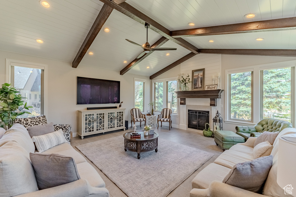 Living room with vaulted ceiling with beams, a glass covered fireplace, baseboards, ceiling fan, and recessed lighting