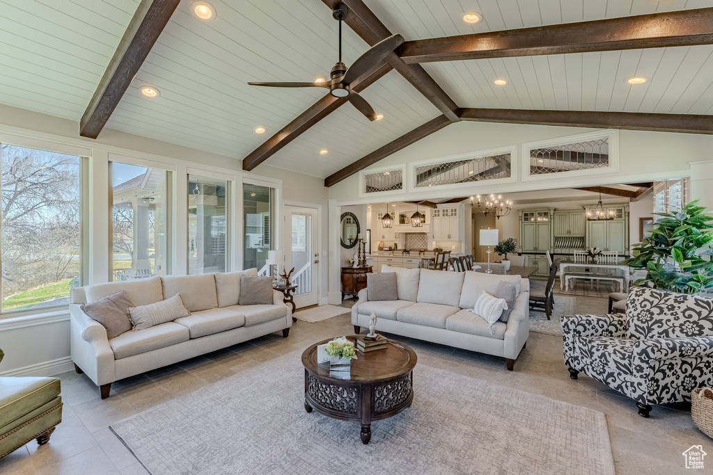 Living room with vaulted ceiling with beams, ceiling fan with notable chandelier, light tile patterned floors, baseboards, and recessed lighting
