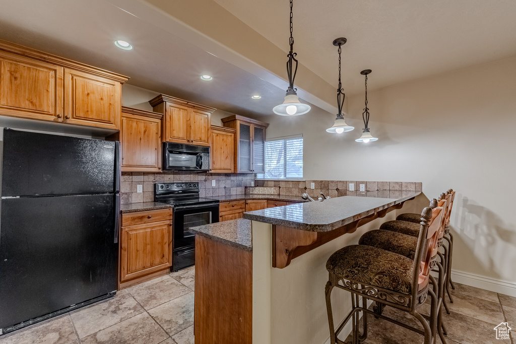 Kitchen featuring a peninsula, a breakfast bar, pendant lighting, black appliances, and backsplash