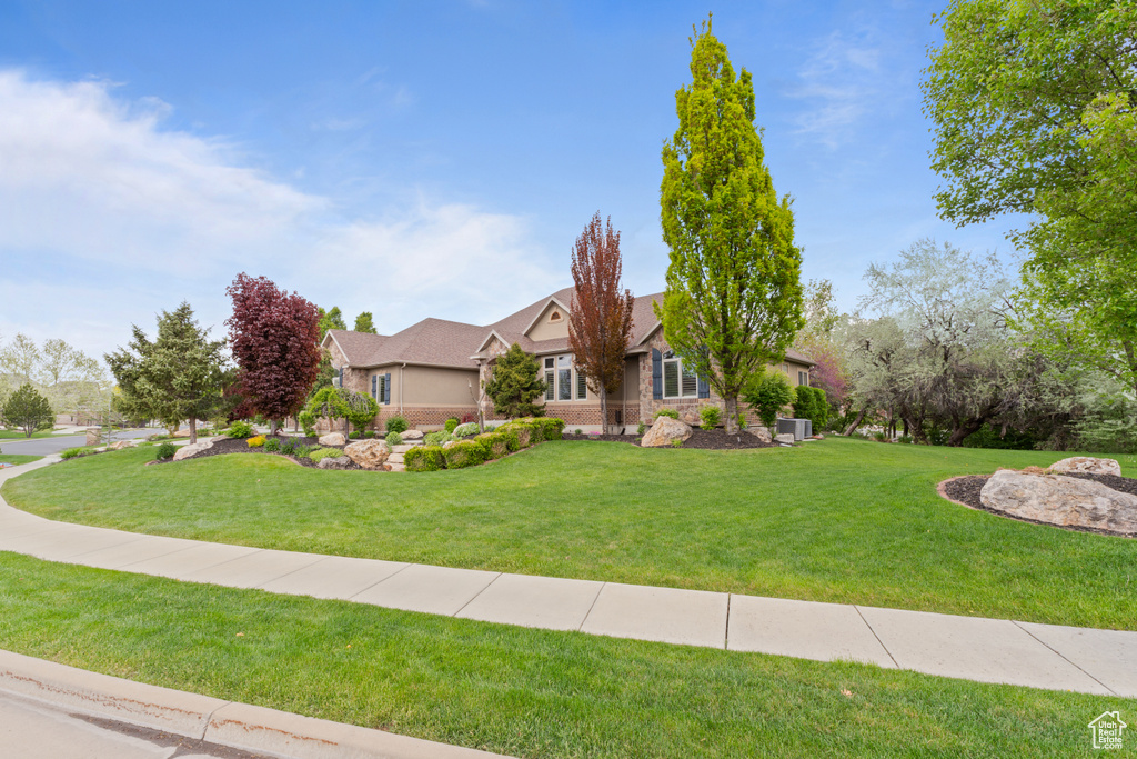 View of front of property with a front yard, cooling unit, and stone siding