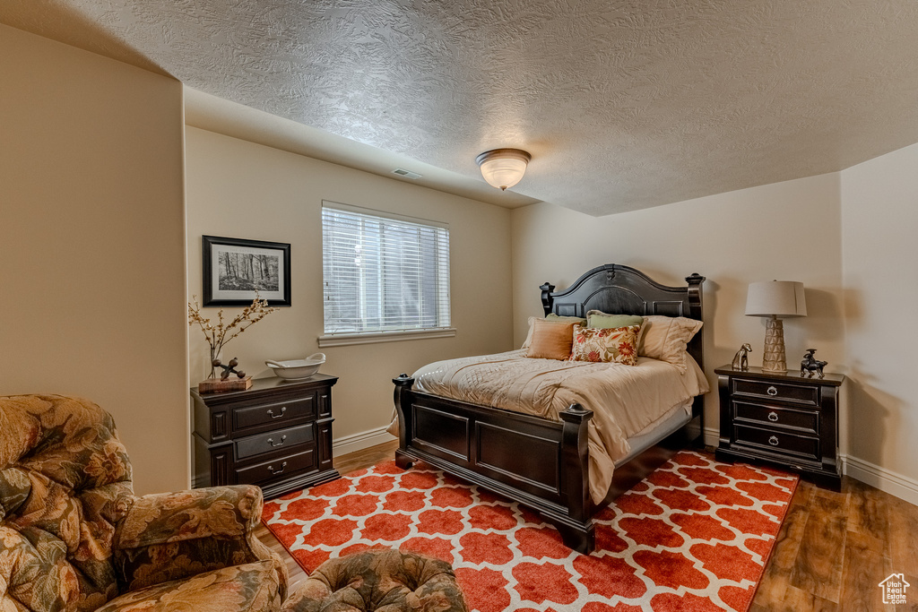 Bedroom with baseboards, visible vents, wood finished floors, and a textured ceiling