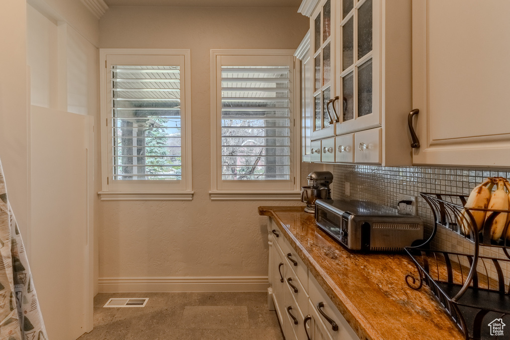 Kitchen featuring tasteful backsplash, glass insert cabinets, baseboards, visible vents, and a toaster