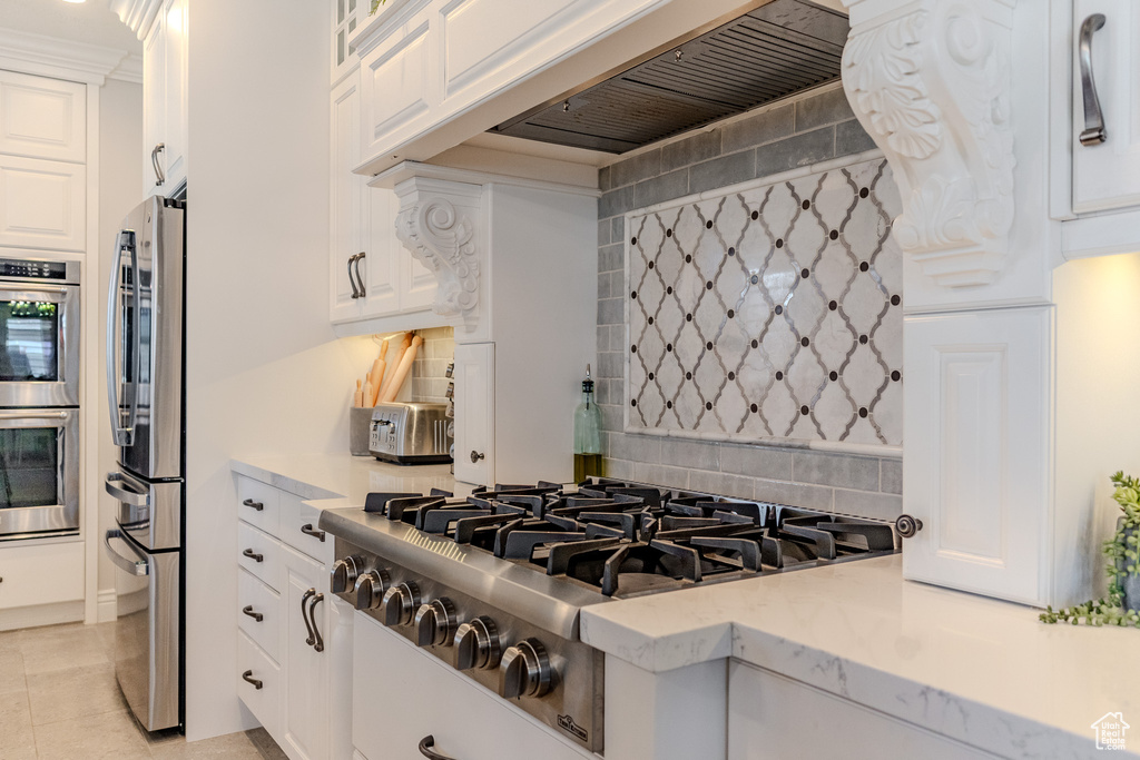 Kitchen featuring custom range hood, white cabinets, stainless steel appliances, and backsplash