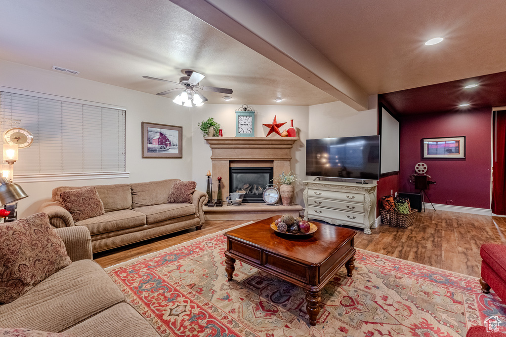 Living room with a ceiling fan, wood finished floors, a glass covered fireplace, visible vents, and beamed ceiling