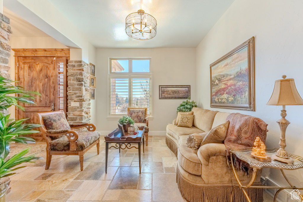 Living room with stone tile flooring, a notable chandelier, and baseboards