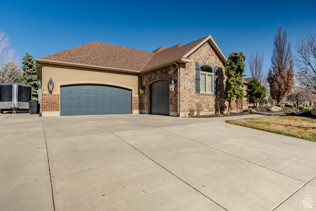 View of front of property with stone siding, an attached garage, concrete driveway, and stucco siding