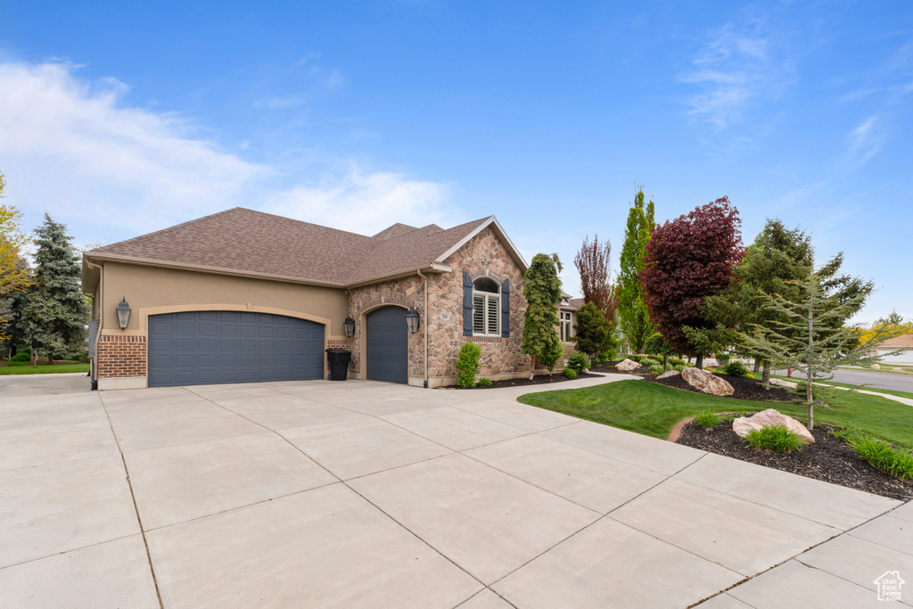 View of front of home with driveway, an attached garage, stucco siding, a front lawn, and brick siding