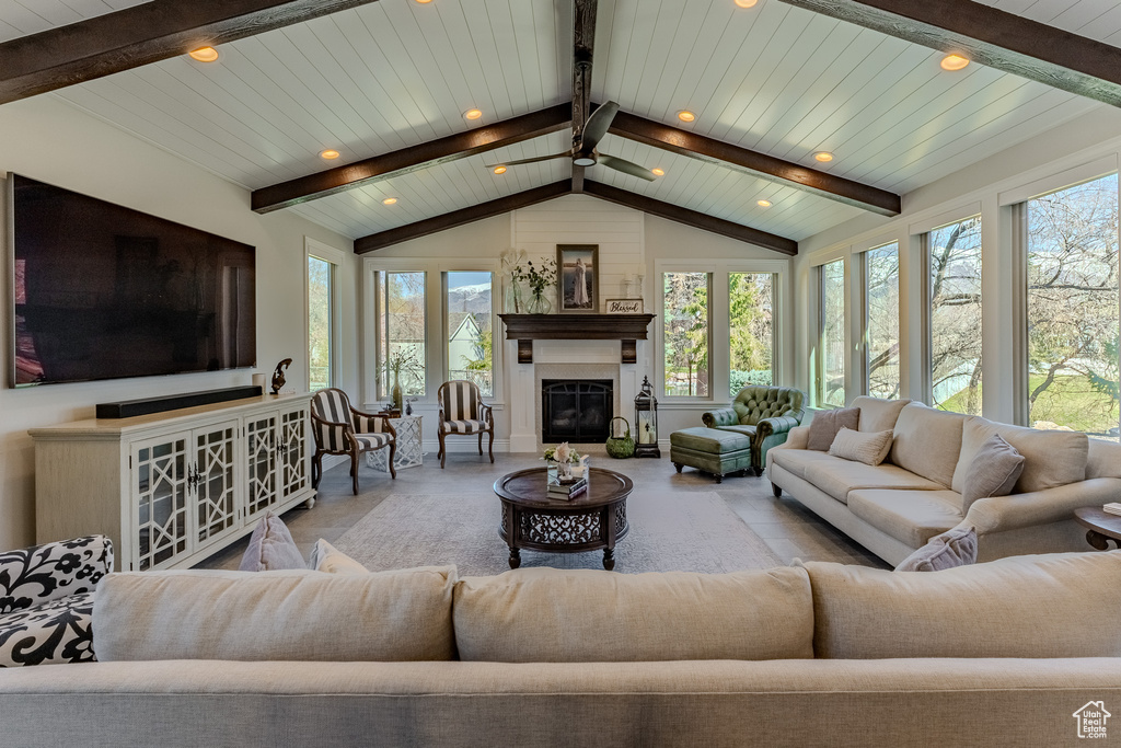 Living area with plenty of natural light, vaulted ceiling with beams, a glass covered fireplace, and a ceiling fan