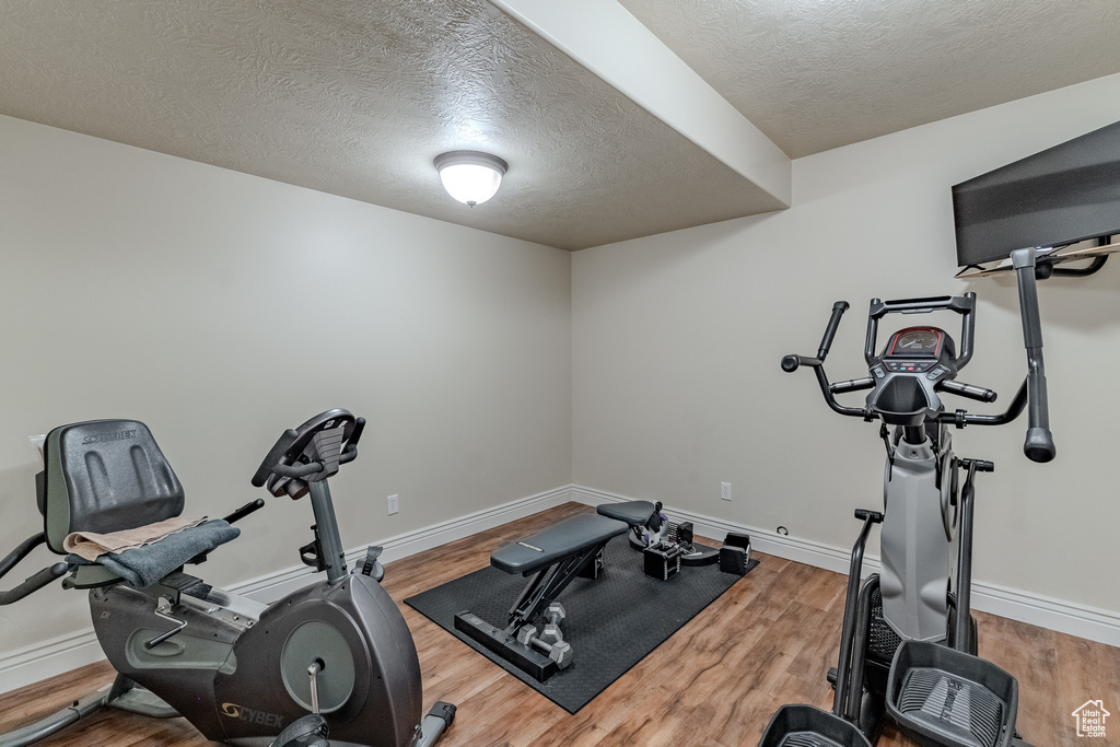 Exercise area featuring baseboards, a textured ceiling, and wood finished floors