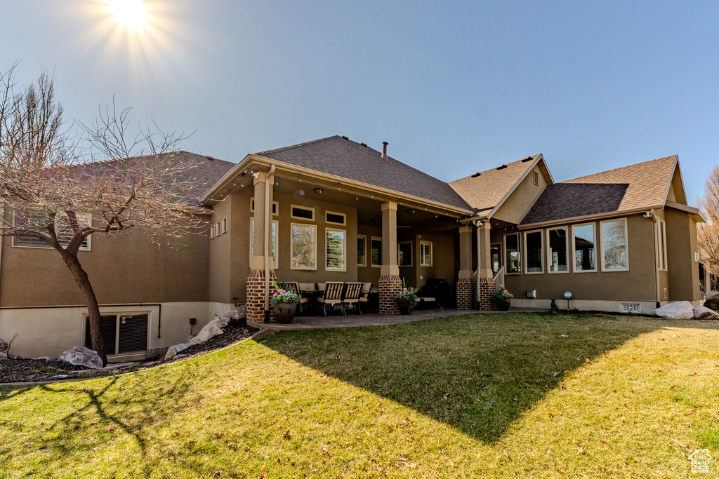Rear view of house featuring a lawn, stucco siding, a patio, and roof with shingles