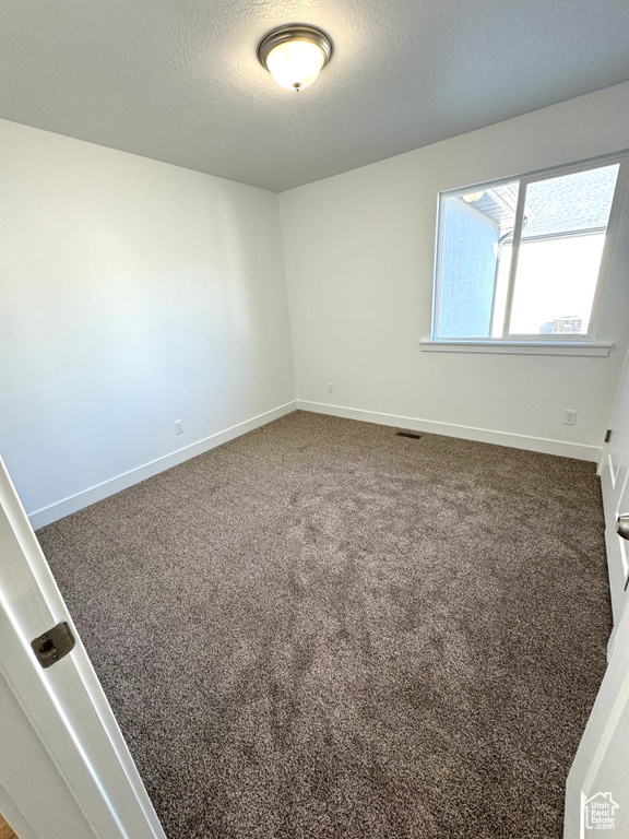 Unfurnished room featuring baseboards, a textured ceiling, visible vents, and carpet