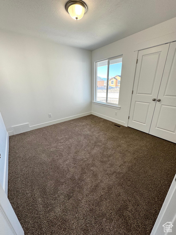 Unfurnished bedroom featuring a textured ceiling, dark colored carpet, and visible vents