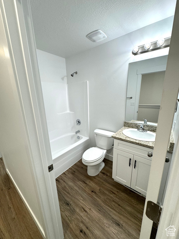 Full bathroom with toilet, vanity, shower / tub combination, wood finished floors, and a textured ceiling