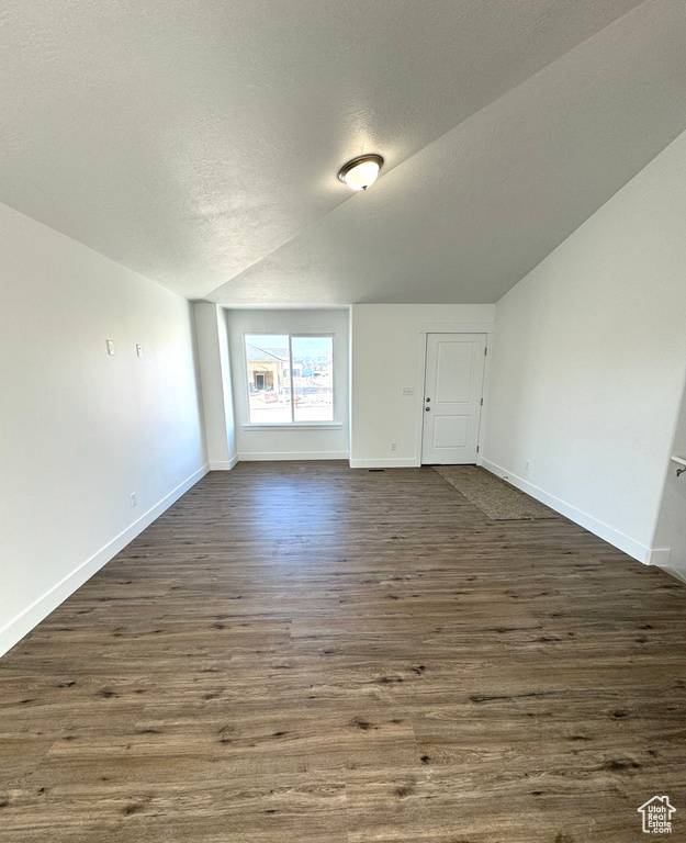 Unfurnished room with baseboards, a textured ceiling, vaulted ceiling, and dark wood finished floors