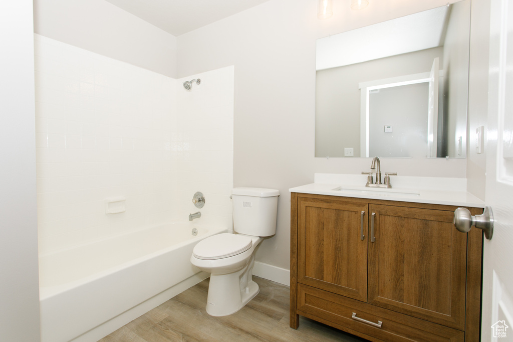 Bathroom with toilet, bathing tub / shower combination, vanity, wood finished floors, and baseboards