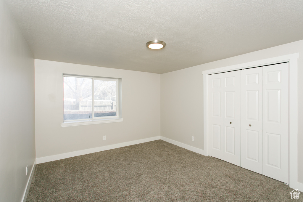 Unfurnished bedroom featuring carpet flooring, baseboards, a closet, and a textured ceiling