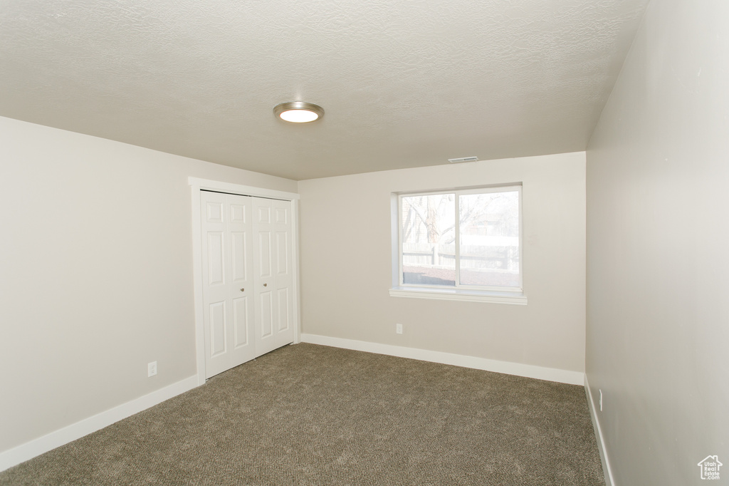 Unfurnished bedroom with carpet flooring, baseboards, a closet, and a textured ceiling