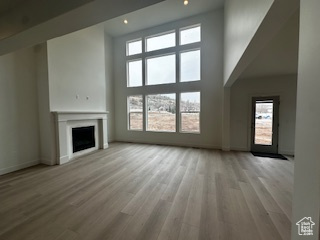Unfurnished living room with baseboards, a fireplace, wood finished floors, and a towering ceiling