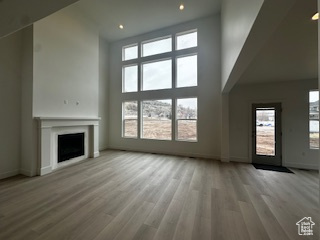 Unfurnished living room with a high ceiling, baseboards, a fireplace, and wood finished floors