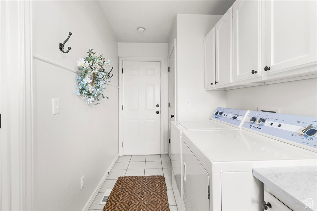 Washroom featuring light tile patterned flooring, baseboards, washing machine and clothes dryer, and cabinet space