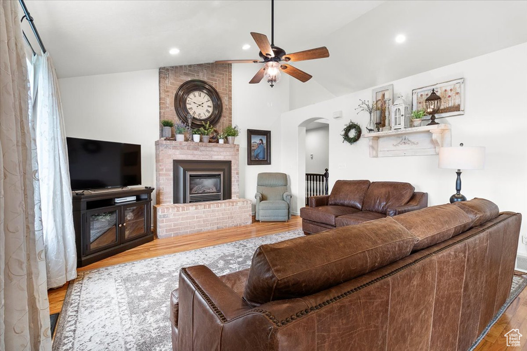 Living room featuring a brick fireplace, ceiling fan, wood finished floors, arched walkways, and lofted ceiling