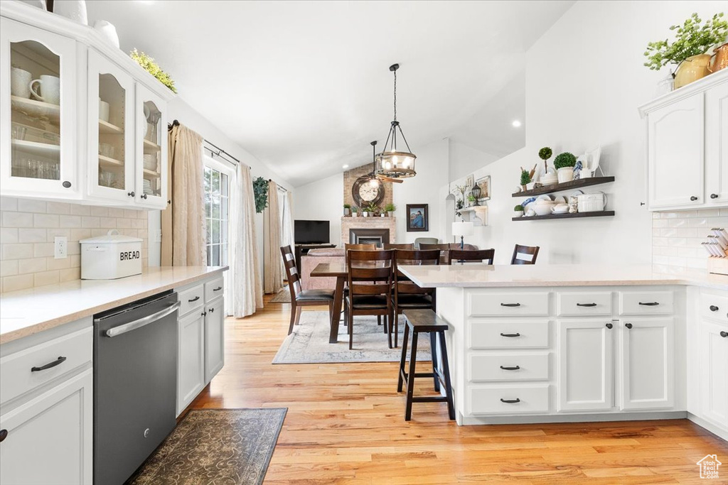 Kitchen featuring light wood finished floors, a kitchen bar, stainless steel dishwasher, lofted ceiling, and white cabinets