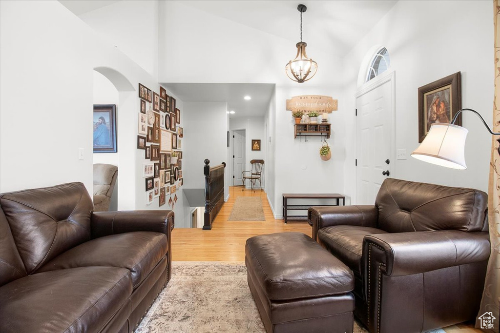 Living area with a notable chandelier, high vaulted ceiling, light wood-style floors, arched walkways, and recessed lighting