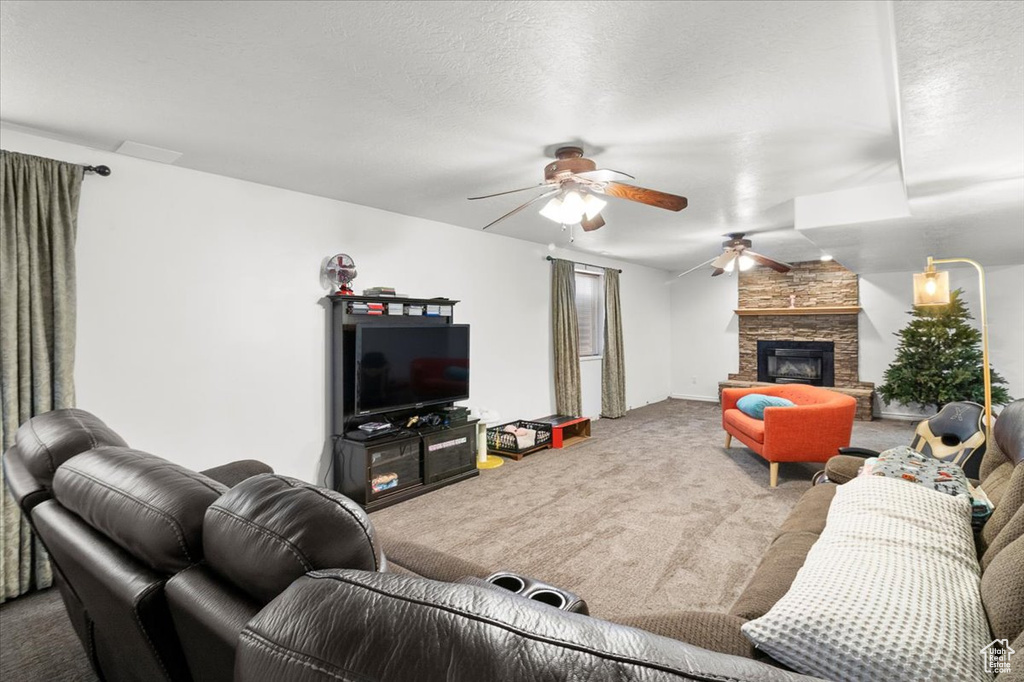 Living room with a fireplace, carpet flooring, ceiling fan, and a textured ceiling