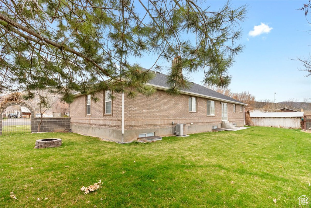 Back of house featuring cooling unit, fence, entry steps, an outdoor fire pit, and brick siding