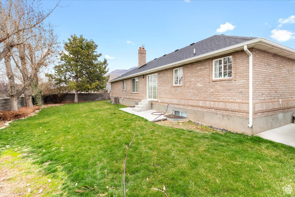Rear view of property featuring fence, entry steps, a chimney, brick siding, and a yard
