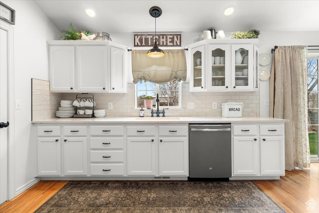 Kitchen featuring stainless steel dishwasher, white cabinetry, wood finished floors, and a sink