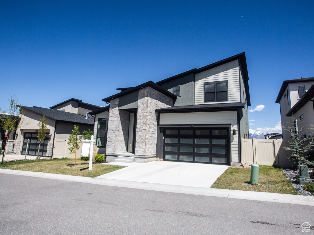 Contemporary home with fence, driveway, an attached garage, and stone siding