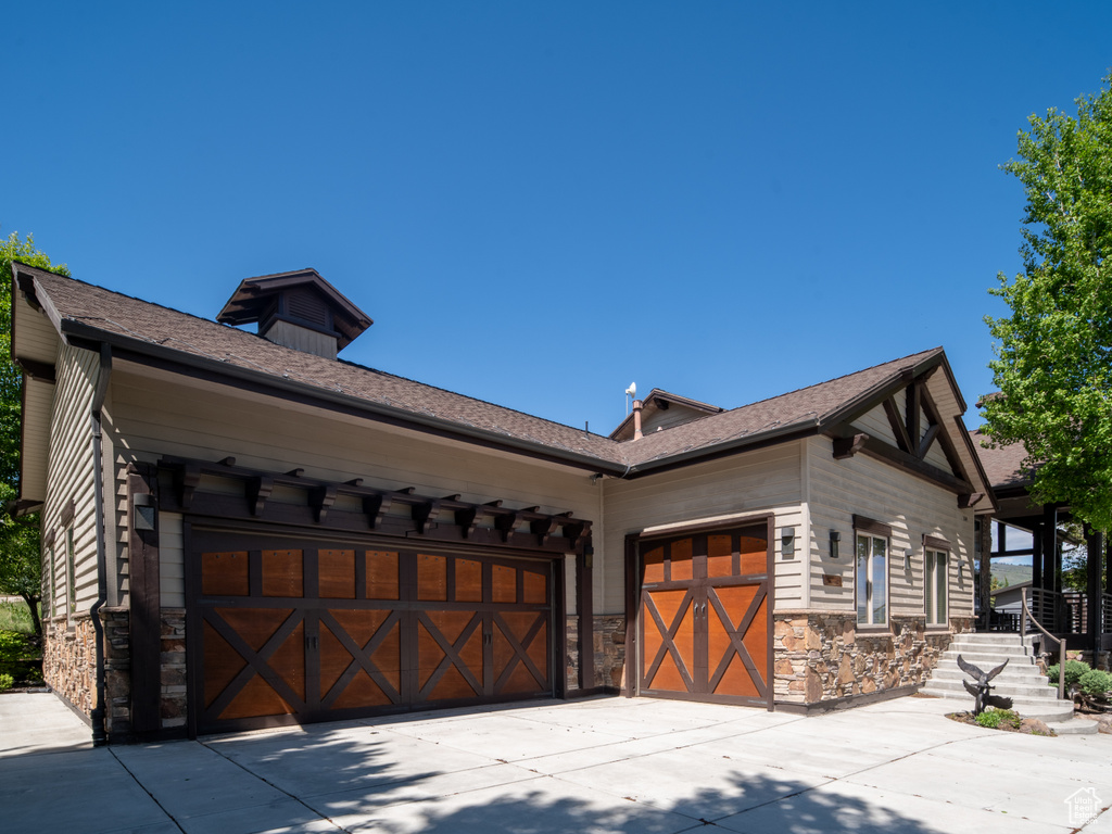 View of side of property featuring stone siding, a garage, and driveway