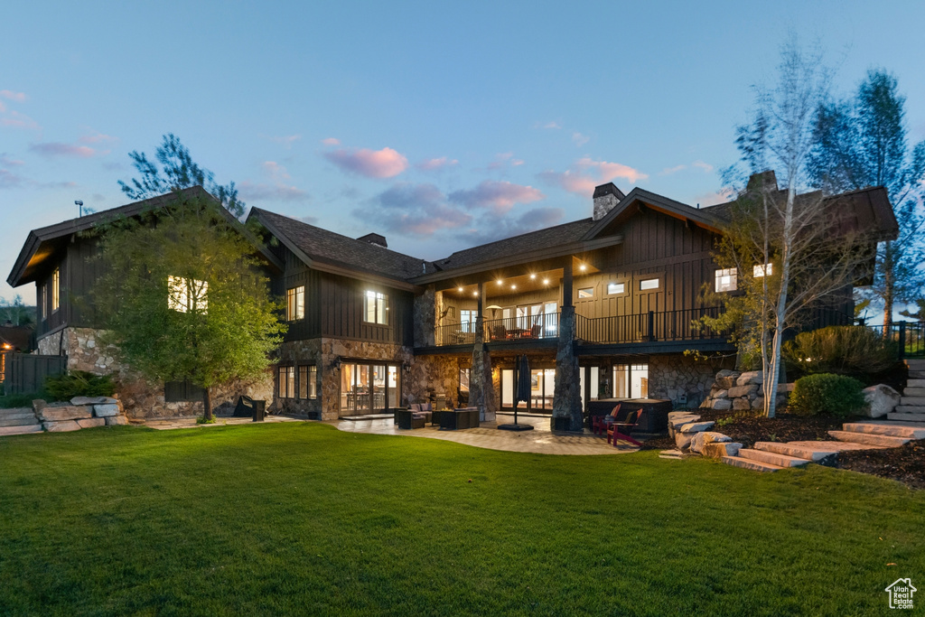 Back of property featuring a balcony, stone siding, and a yard
