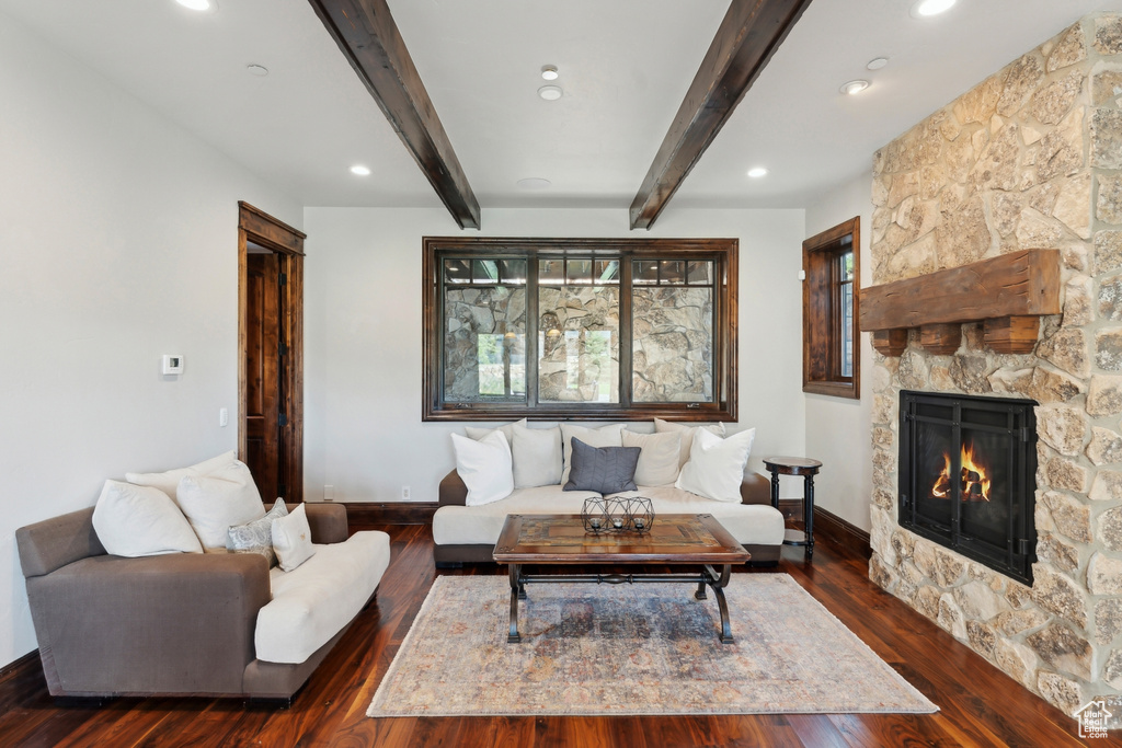 Living area with beamed ceiling, a stone fireplace, dark wood-type flooring, baseboards, and recessed lighting