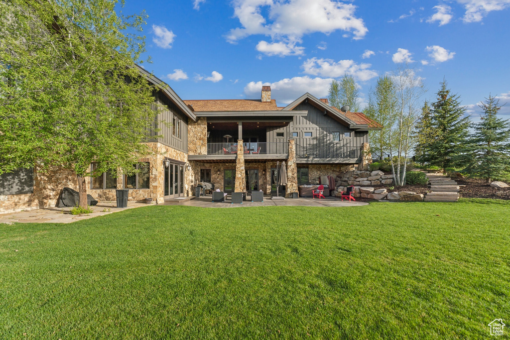 Back of house with a balcony, a patio area, stone siding, board and batten siding, and an outdoor hangout area
