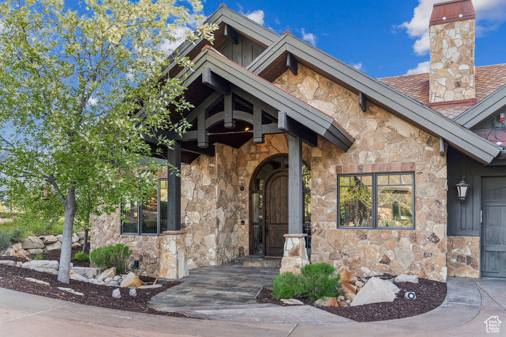Entrance to property featuring stone siding, a chimney, and roof with shingles