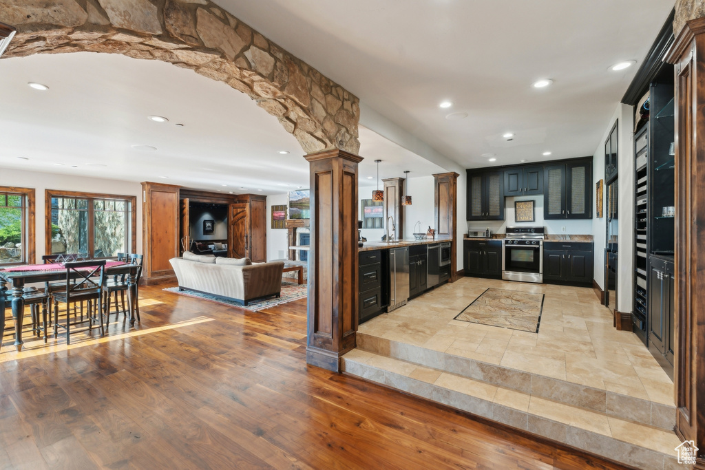 Kitchen with stainless steel appliances, decorative columns, open floor plan, recessed lighting, and light wood-style floors