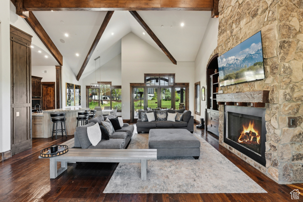 Living room featuring a stone fireplace, dark wood-style flooring, beam ceiling, high vaulted ceiling, and recessed lighting