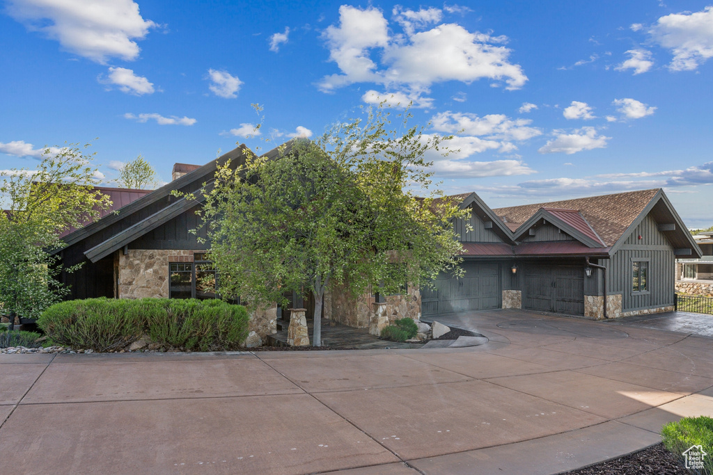View of front of property featuring stone siding, driveway, board and batten siding, and a garage
