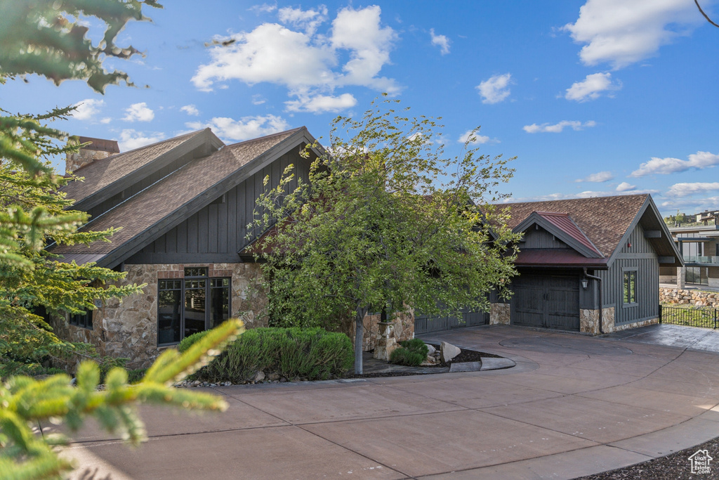 View of front of home featuring stone siding, board and batten siding, concrete driveway, roof with shingles, and an attached garage