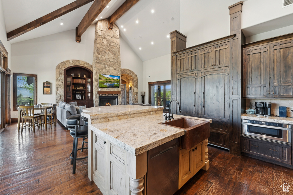 Kitchen with high vaulted ceiling, beamed ceiling, a stone fireplace, stainless steel appliances, and a sink