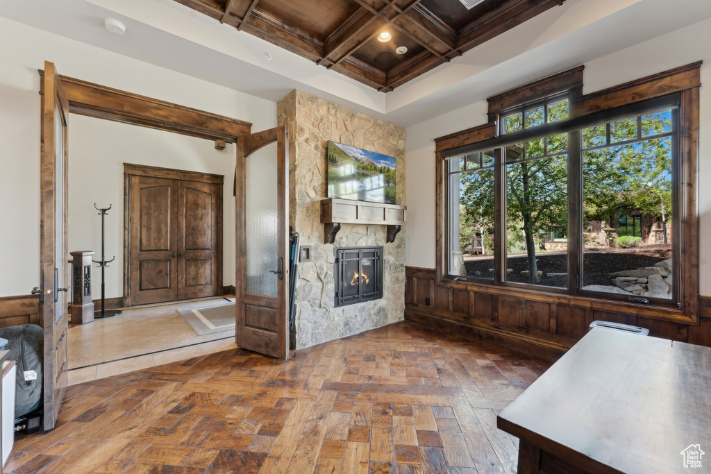 Unfurnished living room with a fireplace, wainscoting, coffered ceiling, and beamed ceiling
