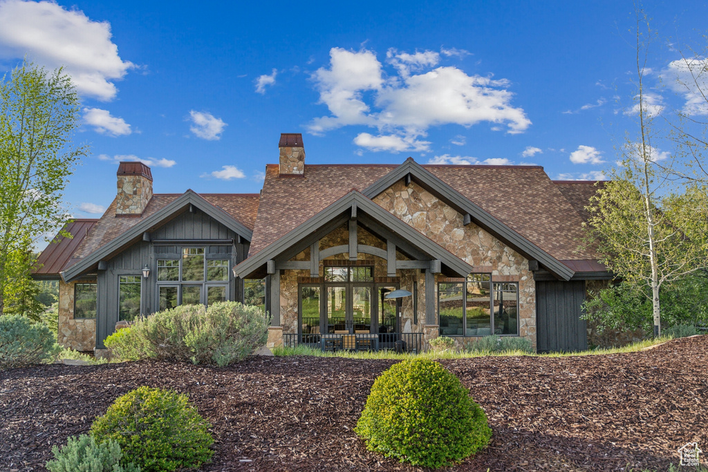 Rear view of house with a chimney, stone siding, and a standing seam roof