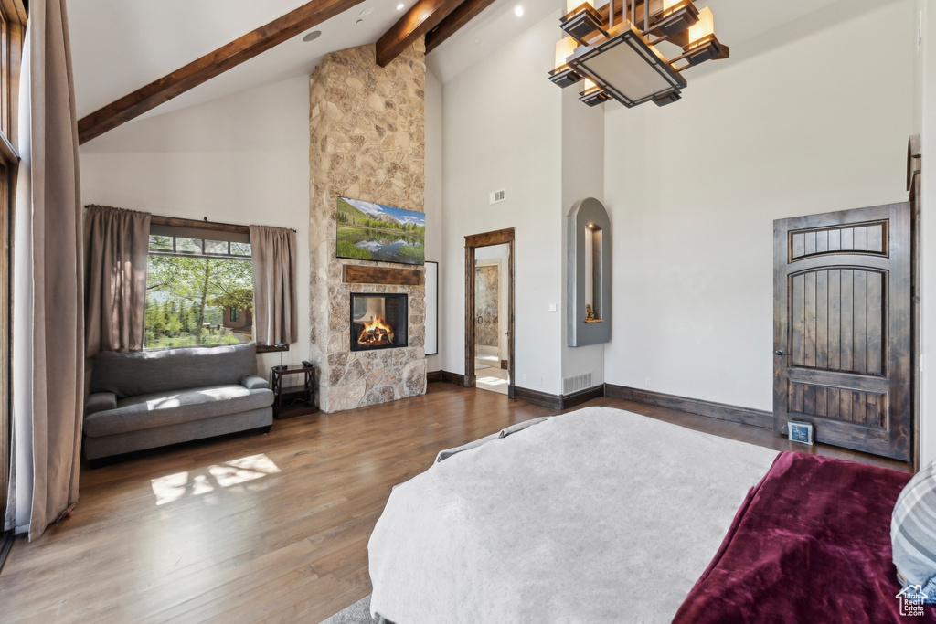 Bedroom featuring high vaulted ceiling, beamed ceiling, a stone fireplace, wood finished floors, and arched walkways