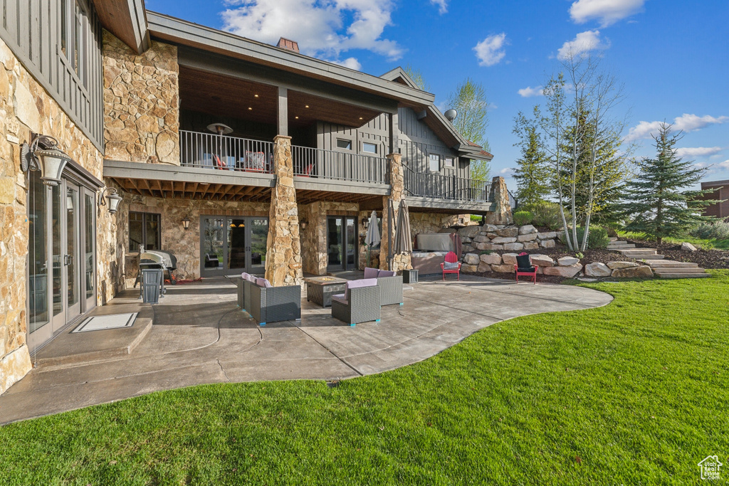 Back of house with a balcony, stone siding, a lawn, a patio area, and an outdoor living space