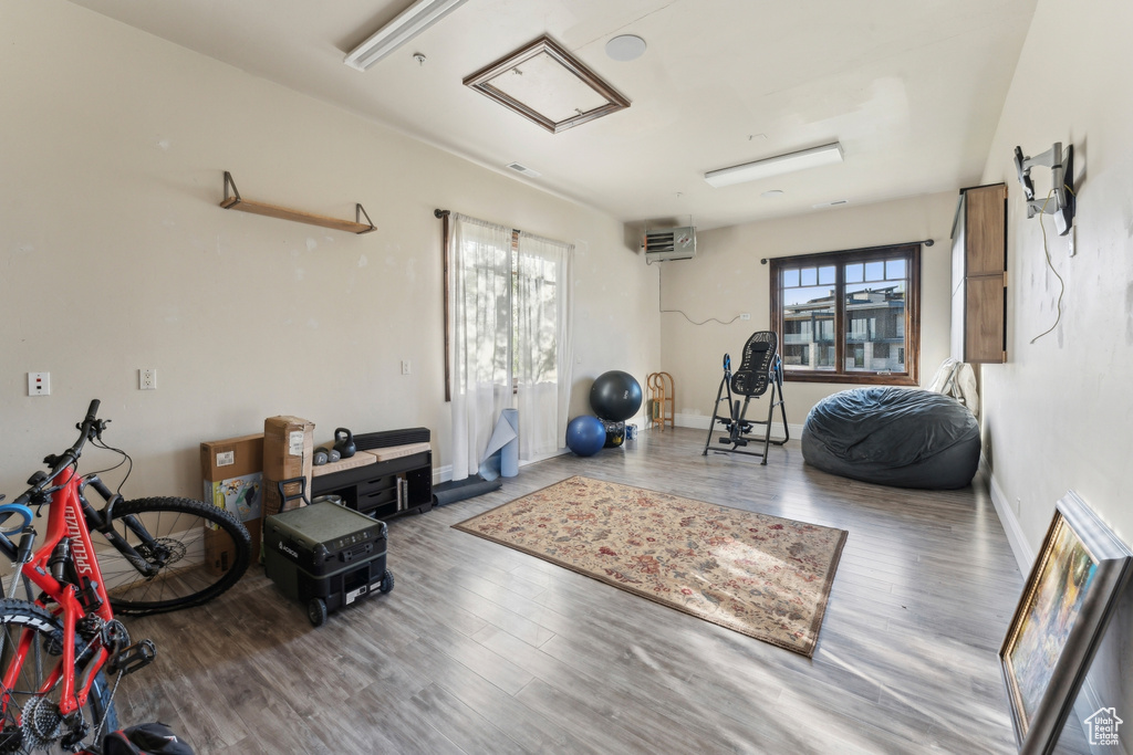 Workout area with wood finished floors, attic access, baseboards, and a wall unit AC